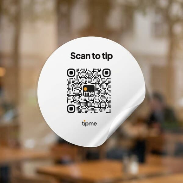 Round tipme QR code sticker on a café glass door, one edge peeling up