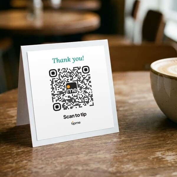 Tent card reading "Thank you!" with a tipme QR code, on a café table next to a latte